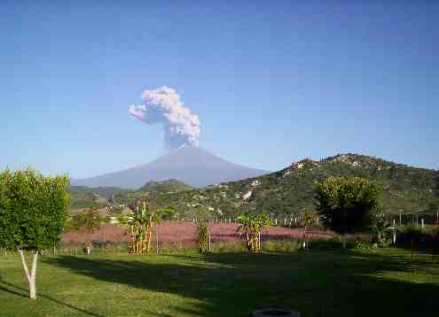 Fotografiá de la zona de campamento, la fotografía se tomó durante el día. Al horizonte se ve el volcán Popocatepetl, tiene una nube de humo sobre si. Mas cerca se ve una montaña, pero no obstruye la vista y en el lugar se ve la zona donde se acampa.