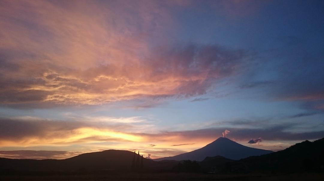 Fotografiá de la zona de campamento, la fotografía se tomó durante el atardecer. Se ve un cielo lleno de colores rojos, amarillos, azules y violetas. Al horizonte se ve la silueta del volcán Popocatepetl