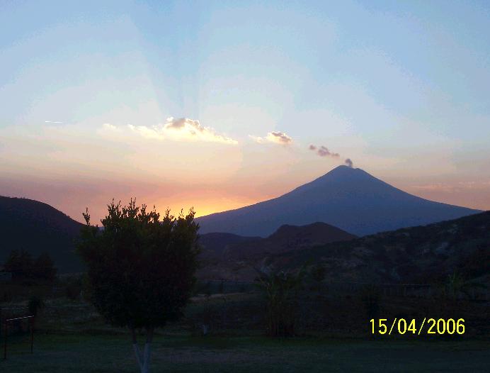 Fotografiá de la zona de campamento, la fotografía se tomó al atarcecer. Se puede ver un cielo que comienza a pintarse de colores rojos, amarillos, azules y violetas. Al horizonte la silueta del volcán Popocatepetl humeando, y mas cerca, se ve la zona de acampar